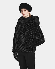 A woman stands against a plain light background, wearing the Rudsak ANASTASIA - 8124804 Black luxury winter coat with a matching hood, faux fur hat, black gloves, and pants.