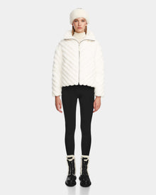 A woman in a white coat and black pants elevates her style with the Rudsak ANASTASIA - 8124804 Iceland, an RDS-certified down womens puffer that seamlessly balances warmth and sophistication.