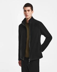 A young man with short dark hair models the Rudsak ARAGON - 6524539 Black full-zip jacket with vegan leather trims over an olive green shirt, standing with one hand in his pocket against a plain white background.