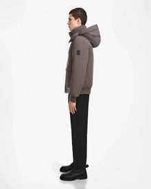 A person with short dark hair stands in profile against a white background, wearing the Rudsak ASH - 6124599 Grey mens down bomber jacket, paired with black pants and boots—ideal for stylish winter wear.