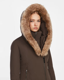 A person wearing the Rudsak AURORE - L123561 Espresso fitted winter parka with a large fur-lined hood looks directly at the camera, expression neutral, set against a plain white background.