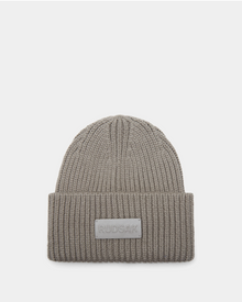 The Rudsak COLIN - 9424518 Cement is a taupe unisex ribbed beanie with a thick folded brim and a rectangular Rudsak patch on the front, shown against a plain white background.