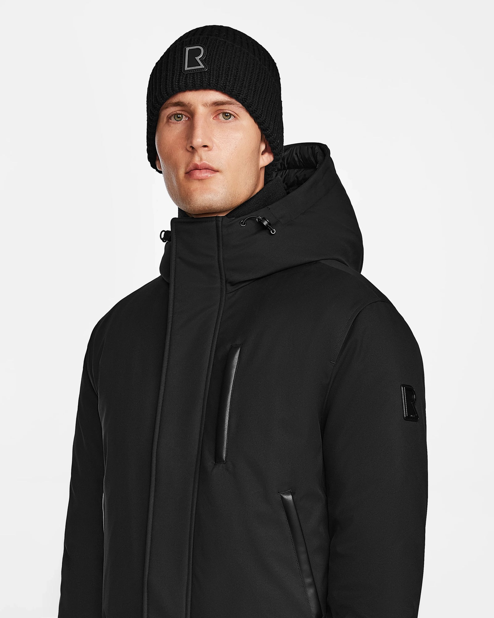A man in a Rudsak DEACON - M123513 Black/Black RDS-certified down puffer winter jacket and a black logo knit beanie stands against a plain white background.