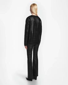 A person with straight blonde hair, seen from behind, wears the Rudsak ELLE - 8524597 Black womens cable knit sweater, black leather pants, and black heeled boots against a plain white background.