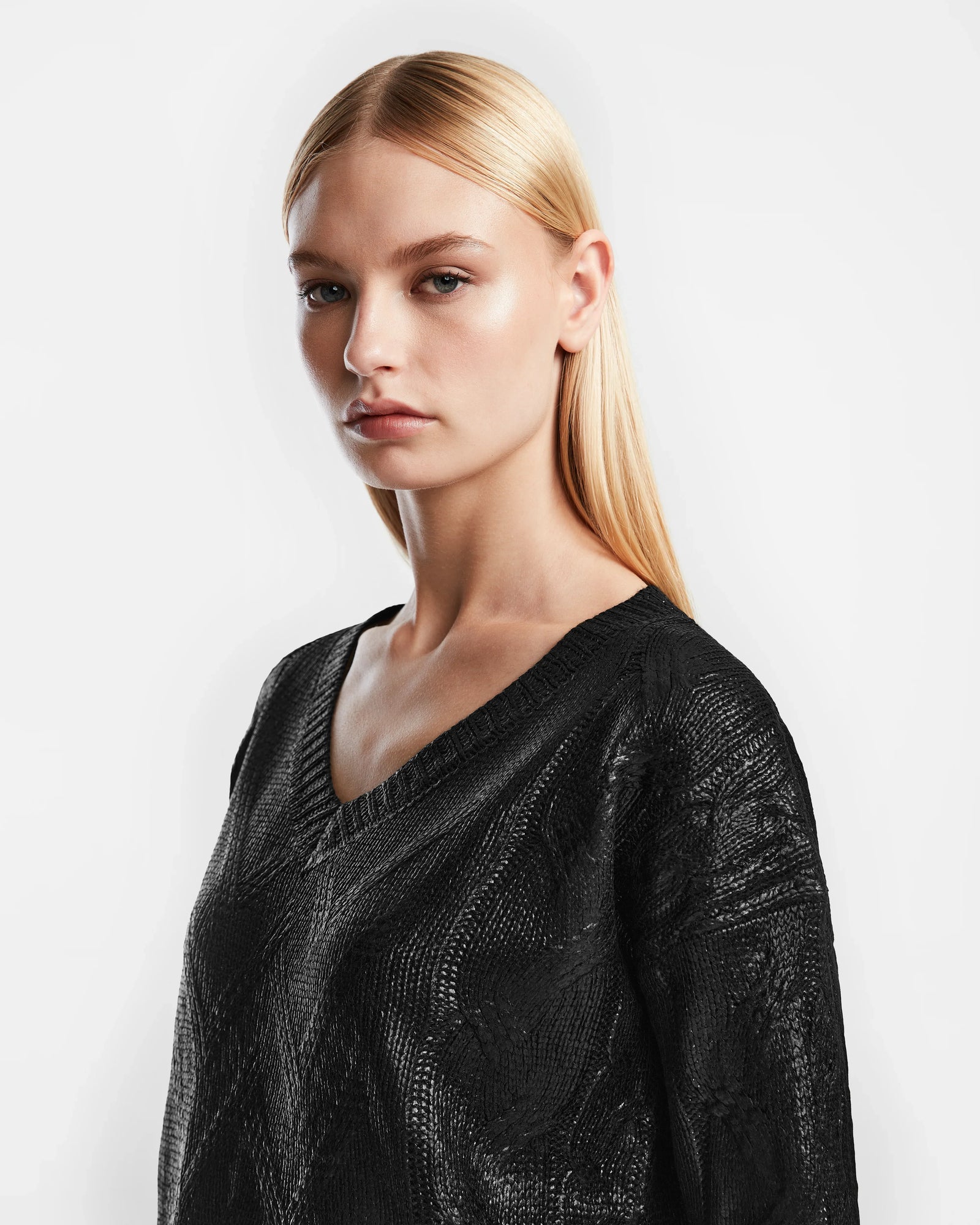 A woman with straight blonde hair and a serious expression wears the Rudsak ELLE - 8524597 Black womens cable knit V-neck sweater, standing against a plain white background.