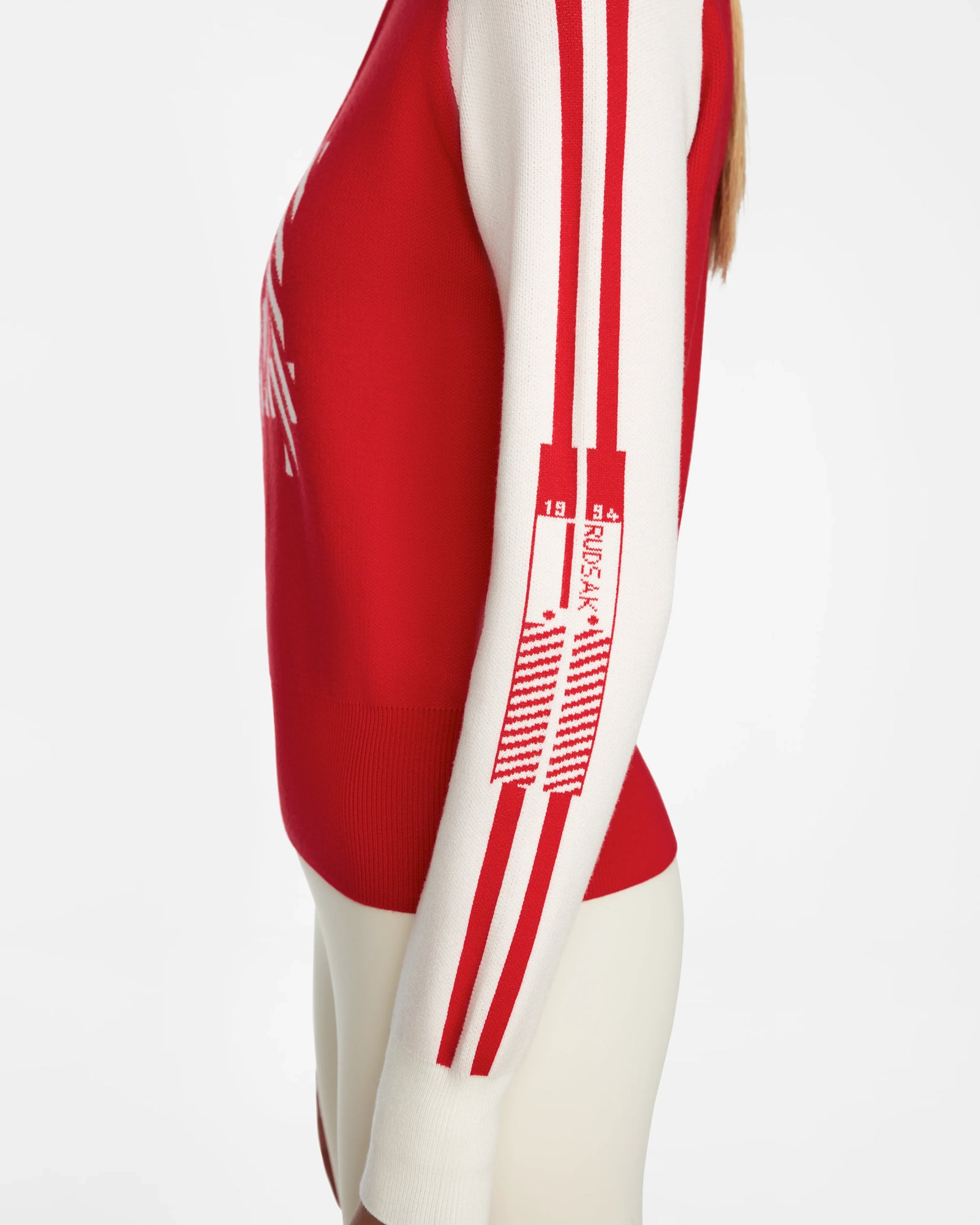 A person wears the Rudsak FANNY - 8524506 Flame Red women’s knit pullover with red and white vertical striped sleeves and a small “RUSSIA 13 14” graphic near the elbow, set against a plain white background.