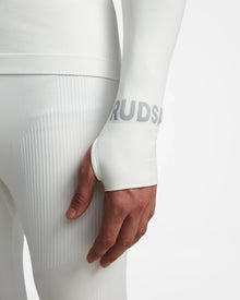 A person wears Rudsaks FRANC - 6524541 Iceland white long-sleeve stretch base layer and matching textured leggings, with a hand through the sleeve’s thumb hole and faint gray text near the wrist visible.