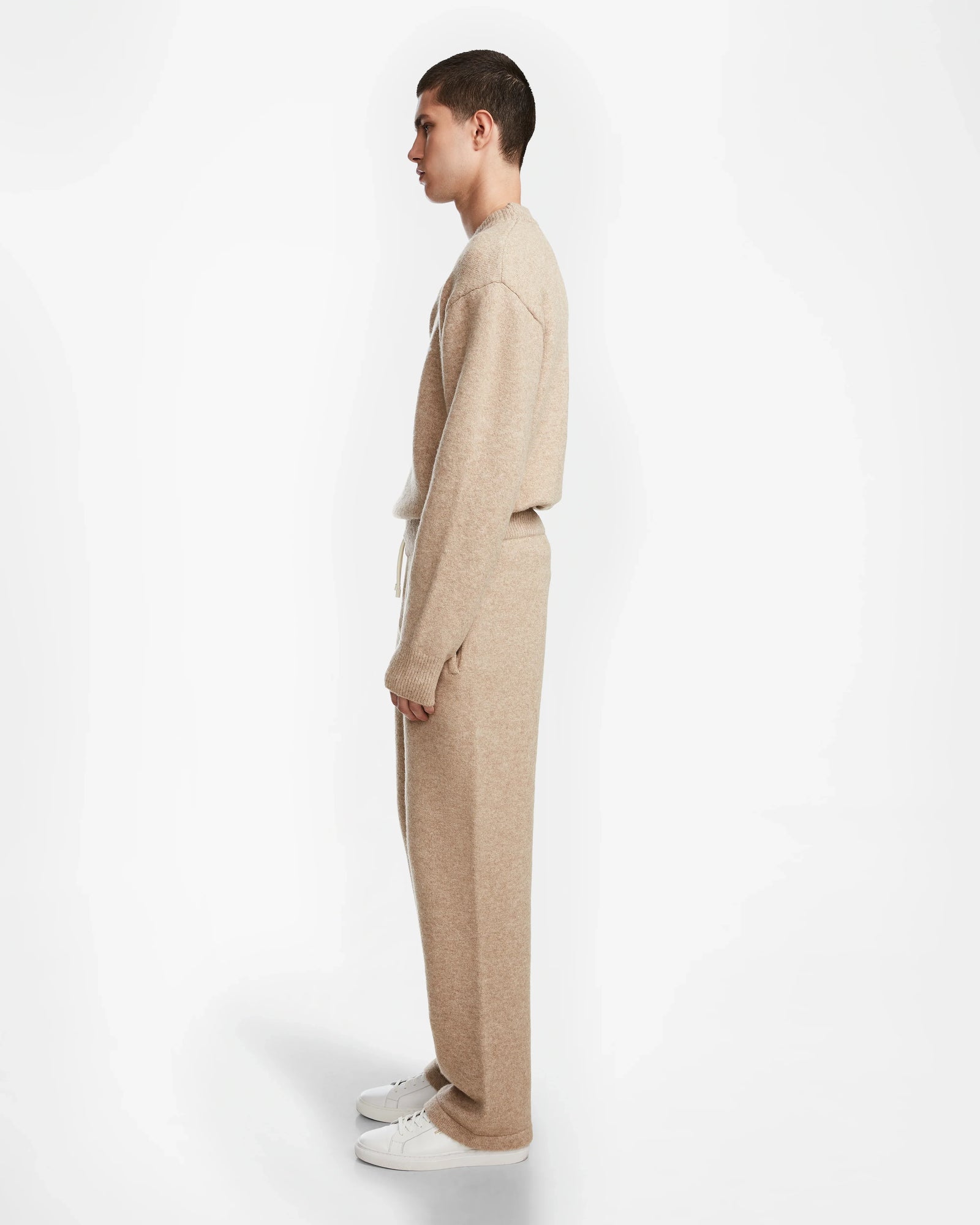 A person in profile wears the Rudsak GEIGER - 9524512 Camel M sweater with relaxed lounge pants and white sneakers, standing against a plain white background.