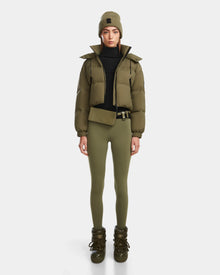 A person faces forward against a plain white background, wearing Rudsak’s KARLEE - 8124721 Loden Green RDS-certified down puffer jacket with matching leggings, a beanie, belt bag, lace-up boots, and a black turtleneck.