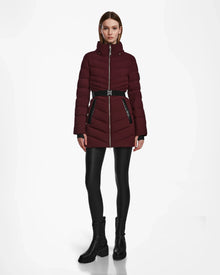 A woman faces forward against a white background, wearing the Rudsak MALAYA M - L123554 Wine belted womens down puffer jacket with herringbone quilting, black leggings, and black ankle boots.