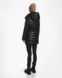 A person wears a tan beanie and the Rudsak MALAYA S - L123510 Black women’s water-resistant down puffer jacket with hood, paired with black leggings and boots, standing facing away on a plain white background.