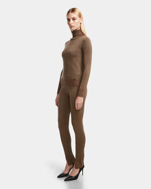 A woman wears the Rudsak MANSUR - 8524624 Antique Bronze textured long-sleeve turtleneck sweater and matching leggings with black heels, posing against a plain white background.