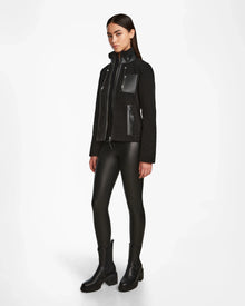 A woman faces slightly to the side wearing Rudsaks MILANA - 8524604 Black zip-up jacket with vegan leather accents, leather-look leggings, and chunky black boots against a plain white background.