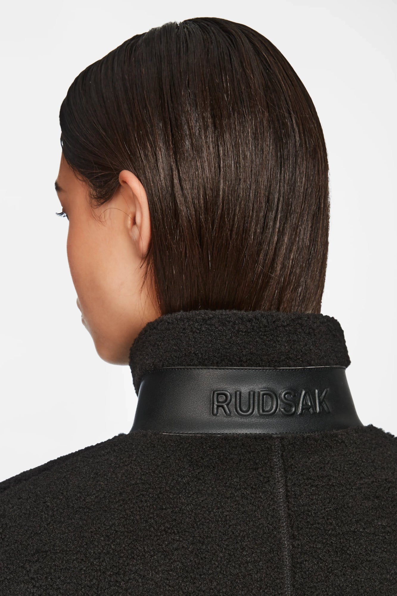 A person with straight, dark brown hair is seen from behind wearing Rudsaks MILANA - 8524604 Black textured coat with a leather collar embossed RUDSAK, layered over a chic teddy sweater for extra warmth and style.