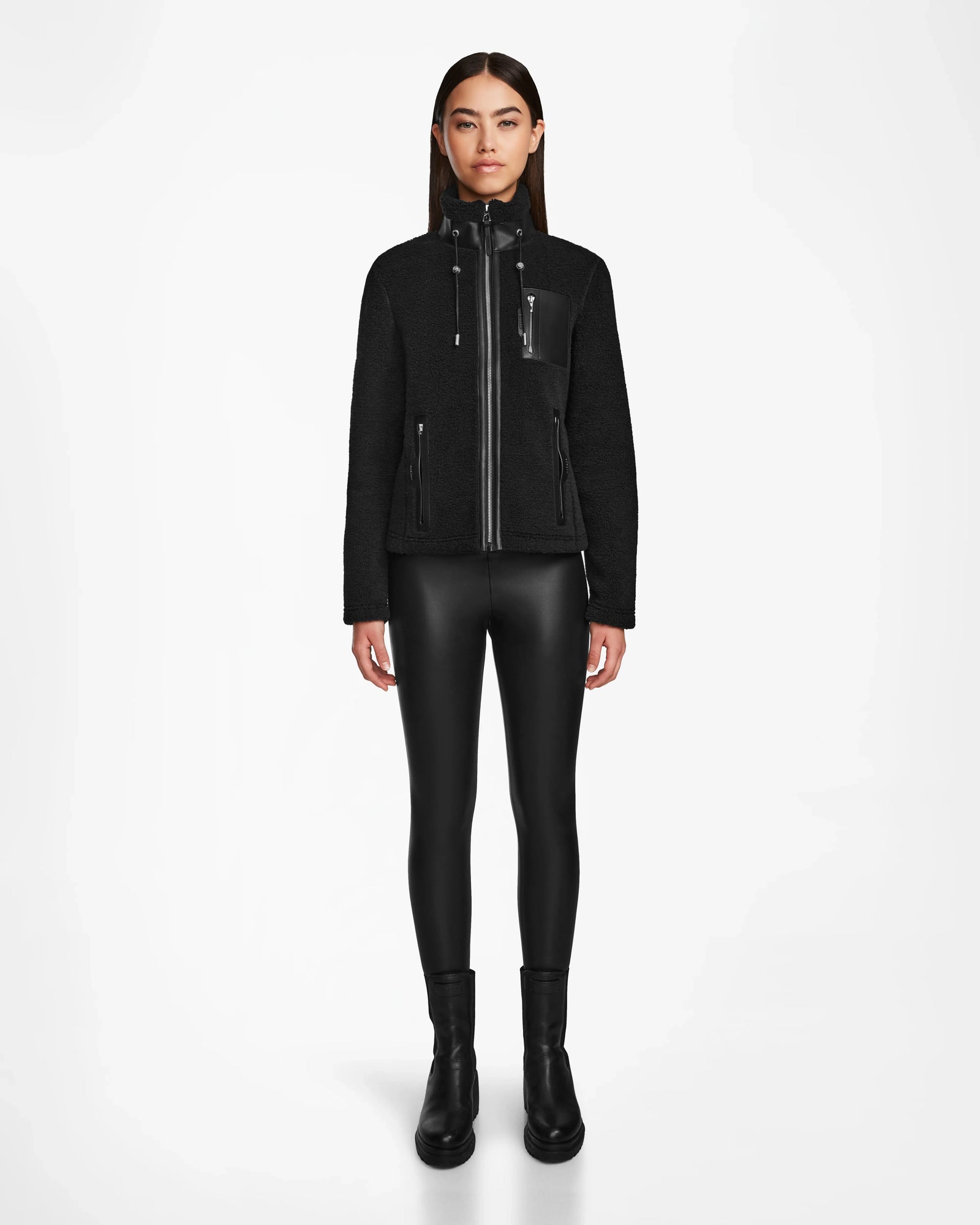A woman faces forward against a white background, wearing the Rudsak MILANA - 8524604 Black zip-up jacket with vegan leather details, black faux leather leggings, and black ankle boots.