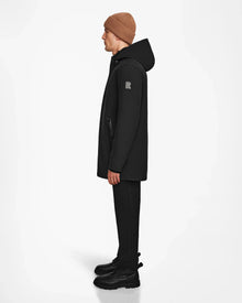 A person wearing a brown beanie, black pants, and black boots stands in profile against a white background, showcasing the Rudsak NATAN - M124519 Black men’s parka with down fill insulation.