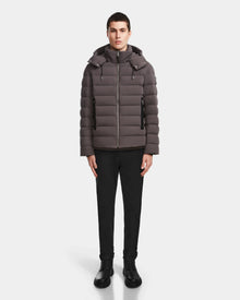 A person stands facing forward, wearing the Rudsak NAVAN - 6124551 Grey men’s quilted down puffer jacket with a hood. The wind and water-repellent, RDS-certified down jacket is set against a plain white background.