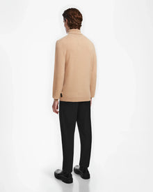 A person with short brown hair, wearing the Rudsak NICOLAS - 6524528 Camel sweater and black pants, stands facing away from the camera against a plain white background.