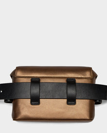 The OFILIA - 8324504 Antique Bronze by Rudsak is a metallic bronze rectangular belt bag with a structured shape, wide black leather strap, and front loops—perfect for elevating any look against a light gray backdrop.