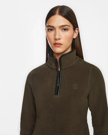 A woman with straight brown hair wears the Rudsak ORCHID - 8524616 Army women’s fitted half-zip pullover sweater with vegan leather trims, standing against a plain white background and looking confidently at the camera.