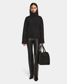 A woman in a relaxed fit turtleneck and leather pants holds the Rudsak PARMI - 8524608 Black bag.