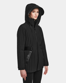 A woman models the Rudsak PETRAS - 8124725 Black quilted jacket with a hood, belted waist, and zippered pockets against a plain light background. She has a neutral expression and gazes slightly to the side.