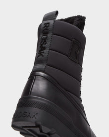 Close-up of the heel of Rudsak’s REAGAN - 6224501 Black men’s winter boots, highlighting a quilted upper, branded pull tab, textured rubber sole, and fuzzy black lining for stylish warmth.