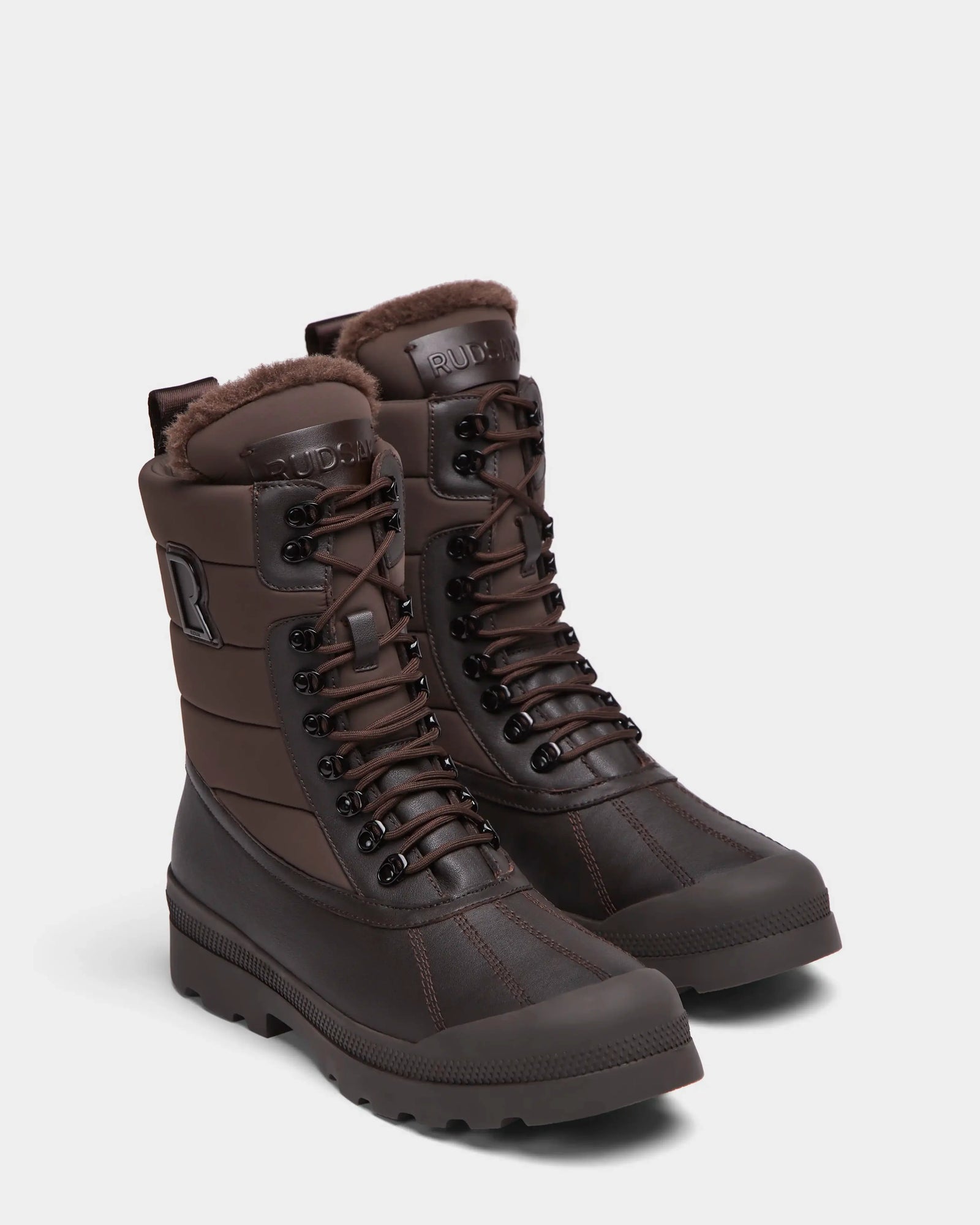 The Rudsak REAGAN - 6224501 Espresso men’s winter boots in dark brown feature lace-up fronts, thick soles, padded uppers, and faux fur lining, shown on a plain white background.