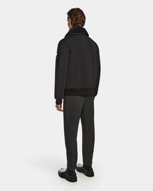 A man stands facing away in a Rudsak REECE - 6124592 Black mens bomber jacket with a shearling collar, paired with gray pants and black boots, set against a plain white background.