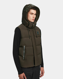 A young man wears the Rudsak REN M - 9123512 Army M, a weather-resistant dark green down puffer vest with an R logo on the chest, zipper front, and pockets, paired with black long sleeves and pants.