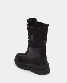 The Rudsak RITA - L222502 Black is a women’s black high-top winter boot with weather-treated leather, thick rubber sole, visible laces, and embossed branding on the side and back heel, displayed on a plain white background.