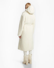 A person with light hair faces away, wearing Rudsaks TINA - 8123578 Iceland ivory textured womens trench coat with a removable hooded bib, matching pants, and chunky off-white boots against a plain white background.
