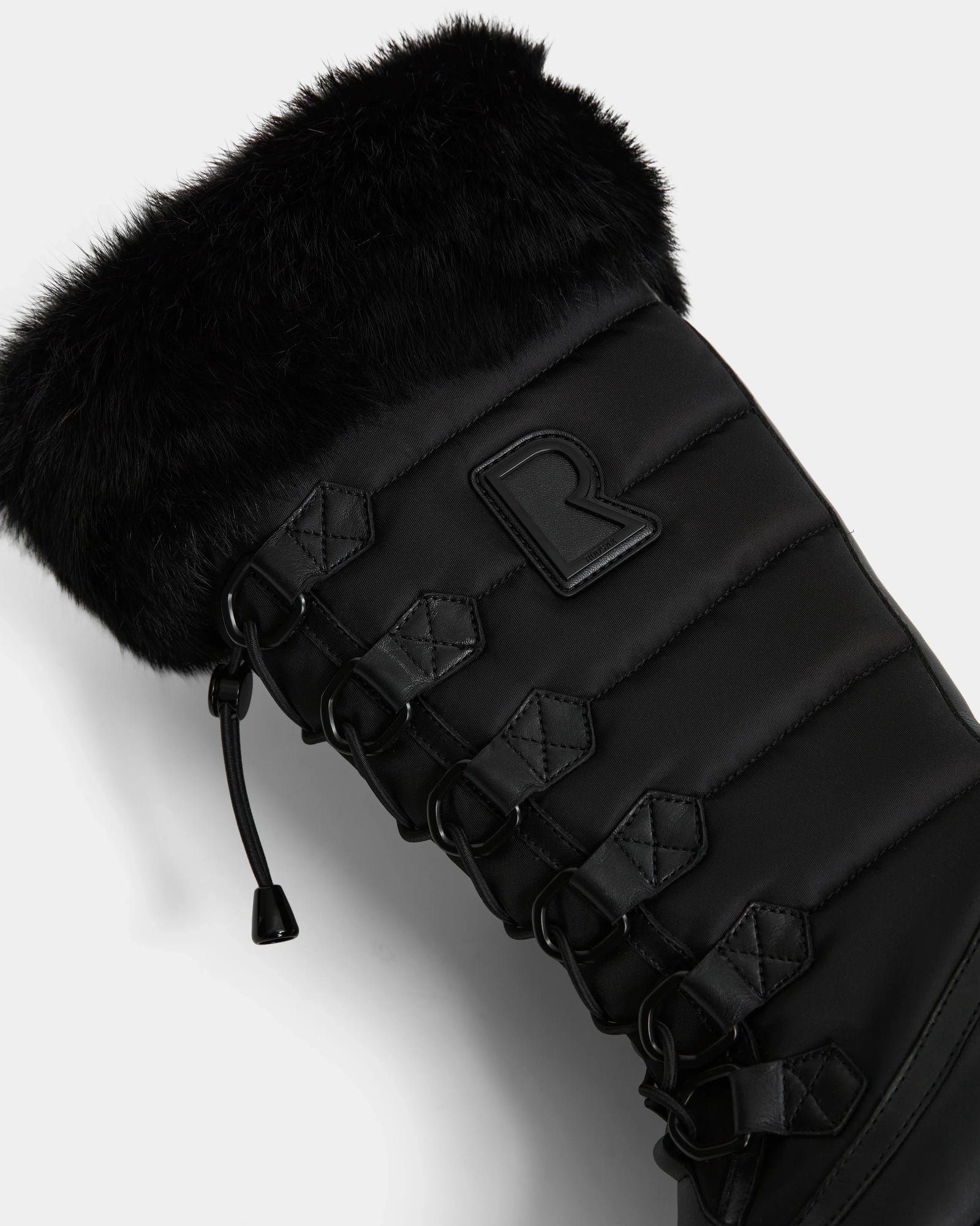 Close-up of the Rudsak WINDY - L224507 Black women's winter boot, featuring faux fur trim, quilted stitching, black laces with metal eyelets, and a raised R logo. Padded fabric offers extra warmth and comfort for cold weather.