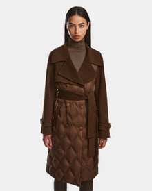 A woman faces forward wearing the Rudsak ZOE - 8124711 Mocha womens long trench coat with quilted details, belt, wide lapels, and buttons over a brown turtleneck. She has straight dark hair. The background is plain white.