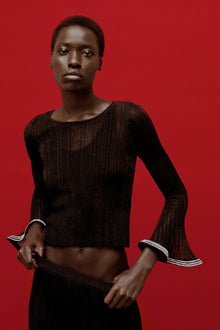Black metallic plissÃ© top with long flared sleeves and striped trim cuffs on red background.