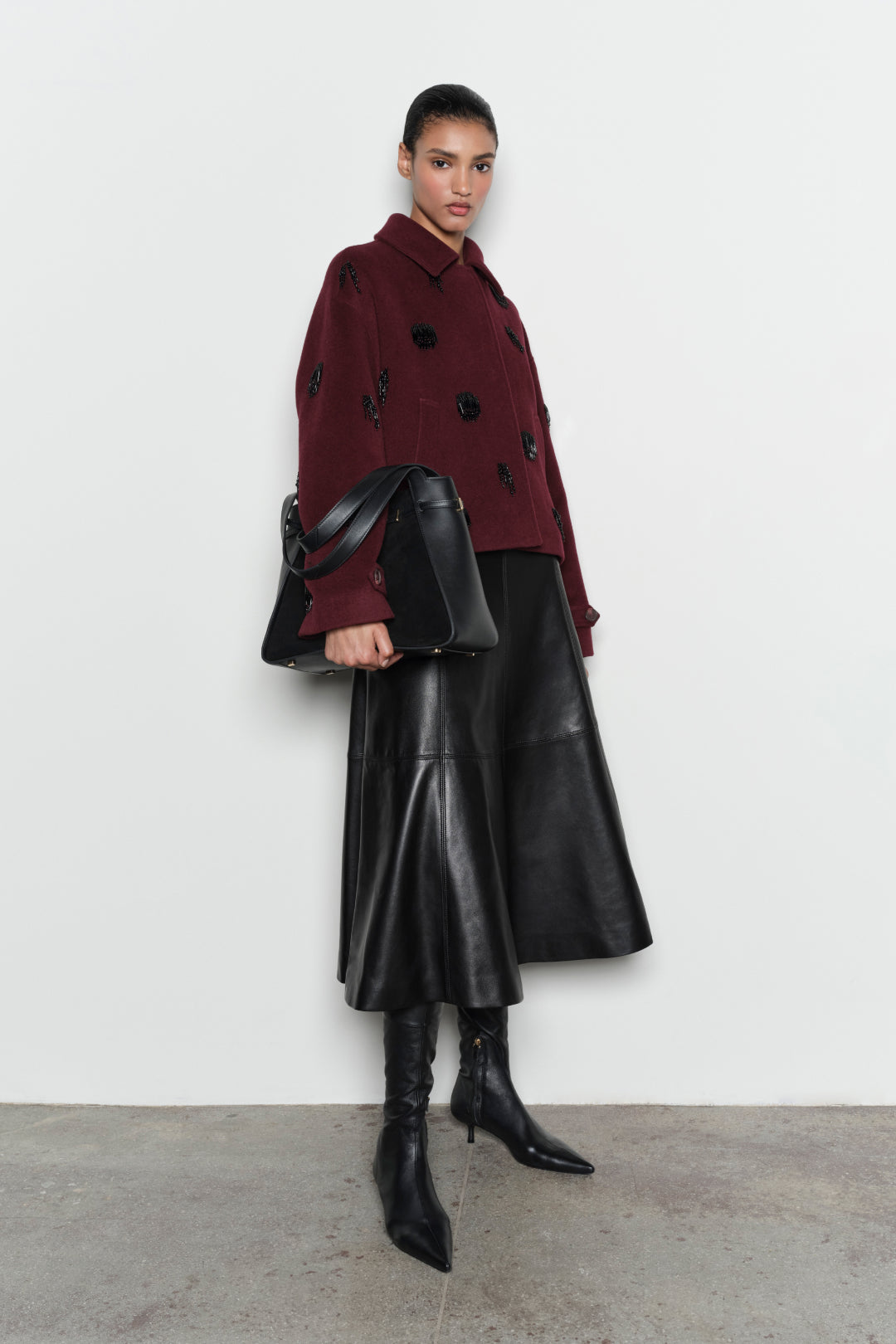 Burgundy wool jacket with black beaded embellishments and collar, worn with black leather midi skirt and boots.