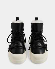 A pair of Rudsak ALEXEY L - L225518 Black women’s leather winter boots with thick white soles, black laces, and visible plush wool lining, shown from the front on a plain white background.