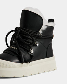 A close-up of the Rudsak ALEXEY L - L225518 Black women’s leather winter boot featuring a thick white sole, silver eyelets, black laces, and plush white faux fur lining visible at the top.