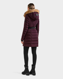 A woman wearing the Rudsak ALISA M - L125586 Bordeaux quilted down parka with faux fur-trimmed hood and vegan leather belt stands facing away from the camera, paired with black leggings and boots against a plain background.