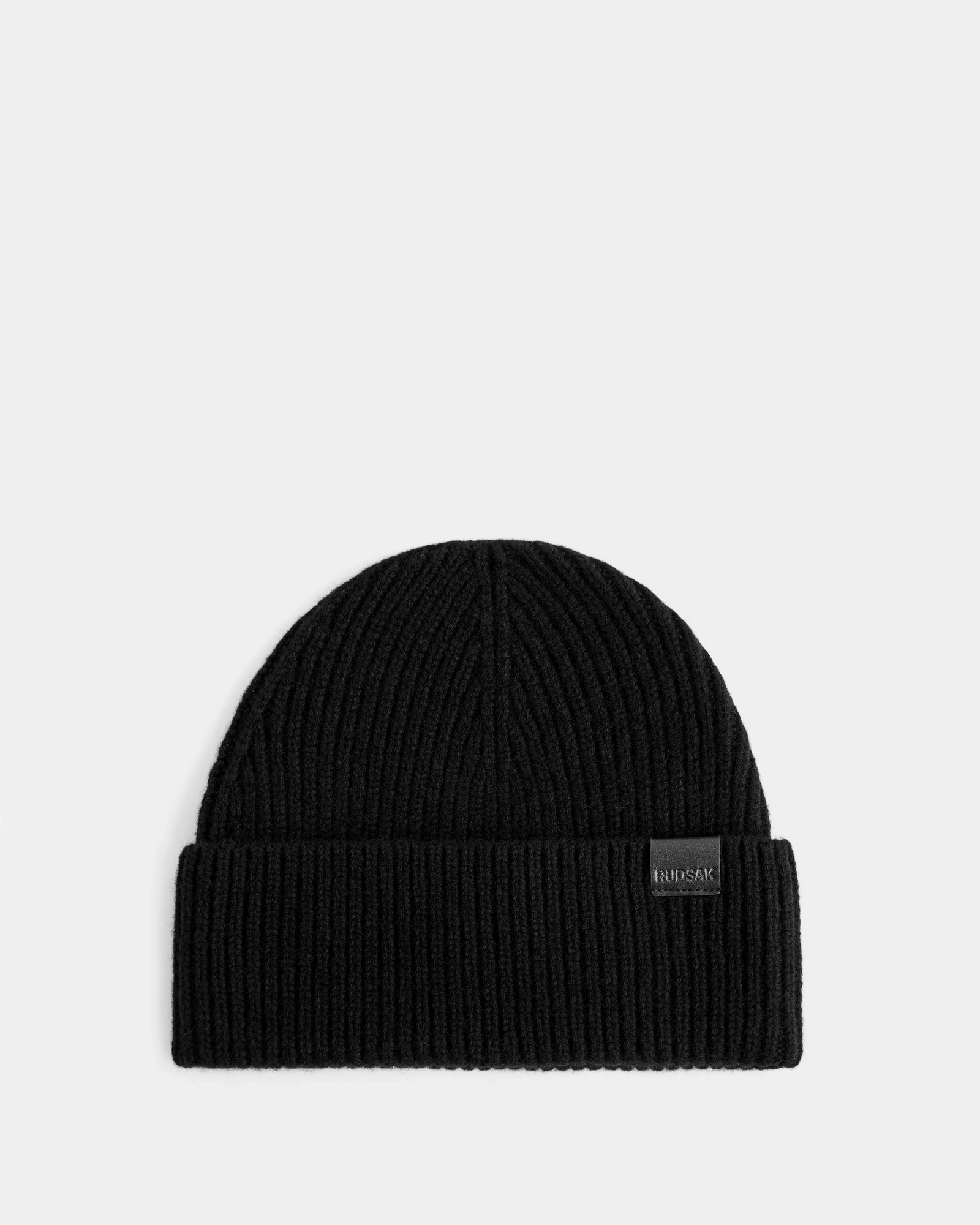 The Rudsak ANDREY - U425507 Black beanie is a unisex, black rib-knit hat with a folded brim and small front rectangular label, shown on a plain light gray background.