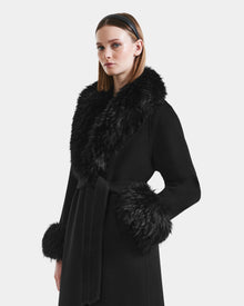 A woman wearing the Rudsak ARTIS - L125575 Black wool coat with a wide faux fur collar and cuffs stands against a plain light background, her straight brown hair held back with a headband and a neutral expression on her face.