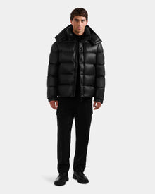A man faces forward in a shiny black Rudsak BRAYDEN S - M125525 quilted down puffer jacket, paired with black pants and shoes, set against a plain light gray background.