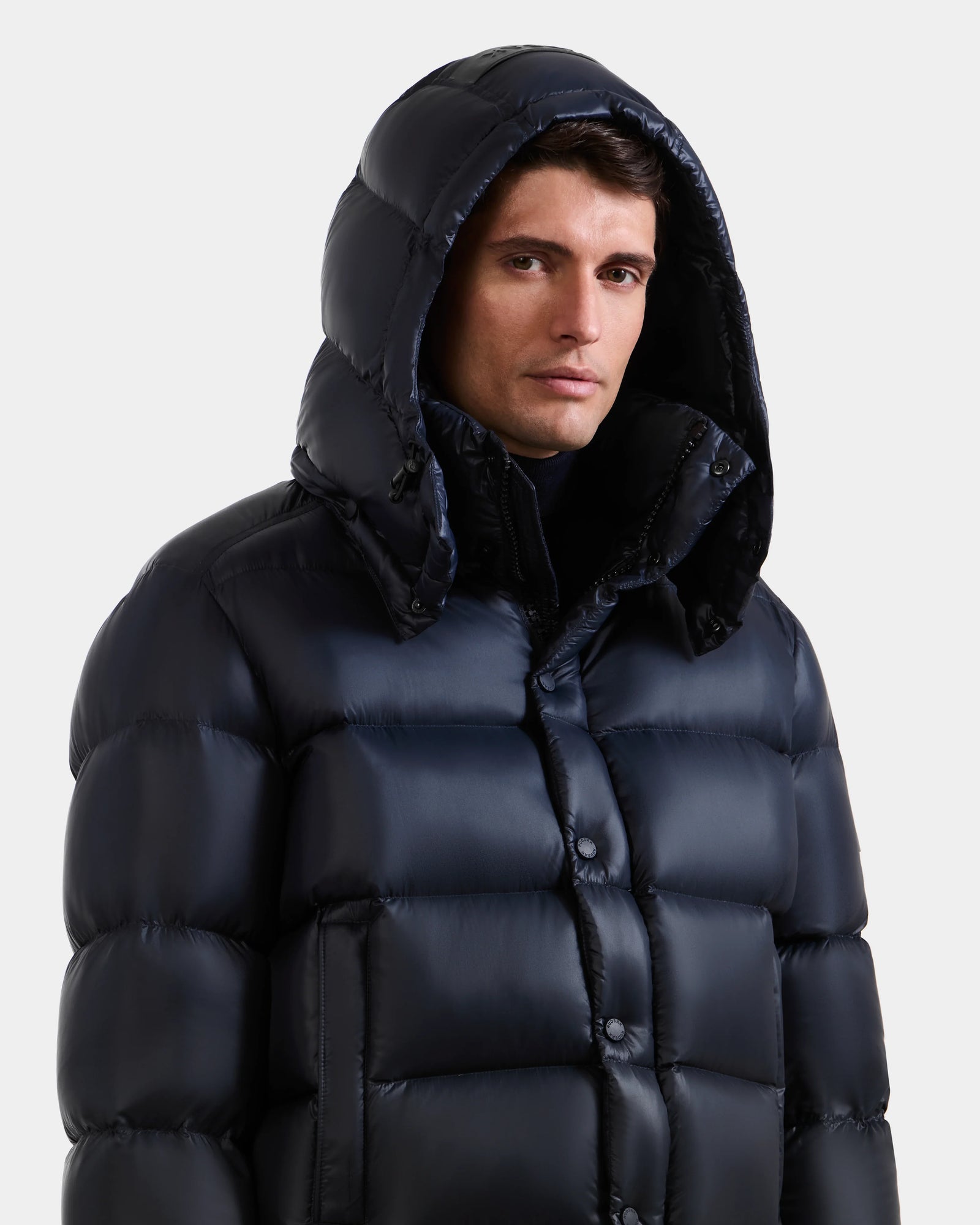 A man wears the BRAYDEN S - M125525 Navy quilted down puffer jacket by Rudsak with the hood up, looking slightly to the side against a plain light background.