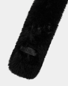 A close-up of the Rudsak CARMY - L425534 Black women’s faux-fur scarf, highlighted by a rectangular embossed patch, showcases its plush warmth against a plain light gray background.