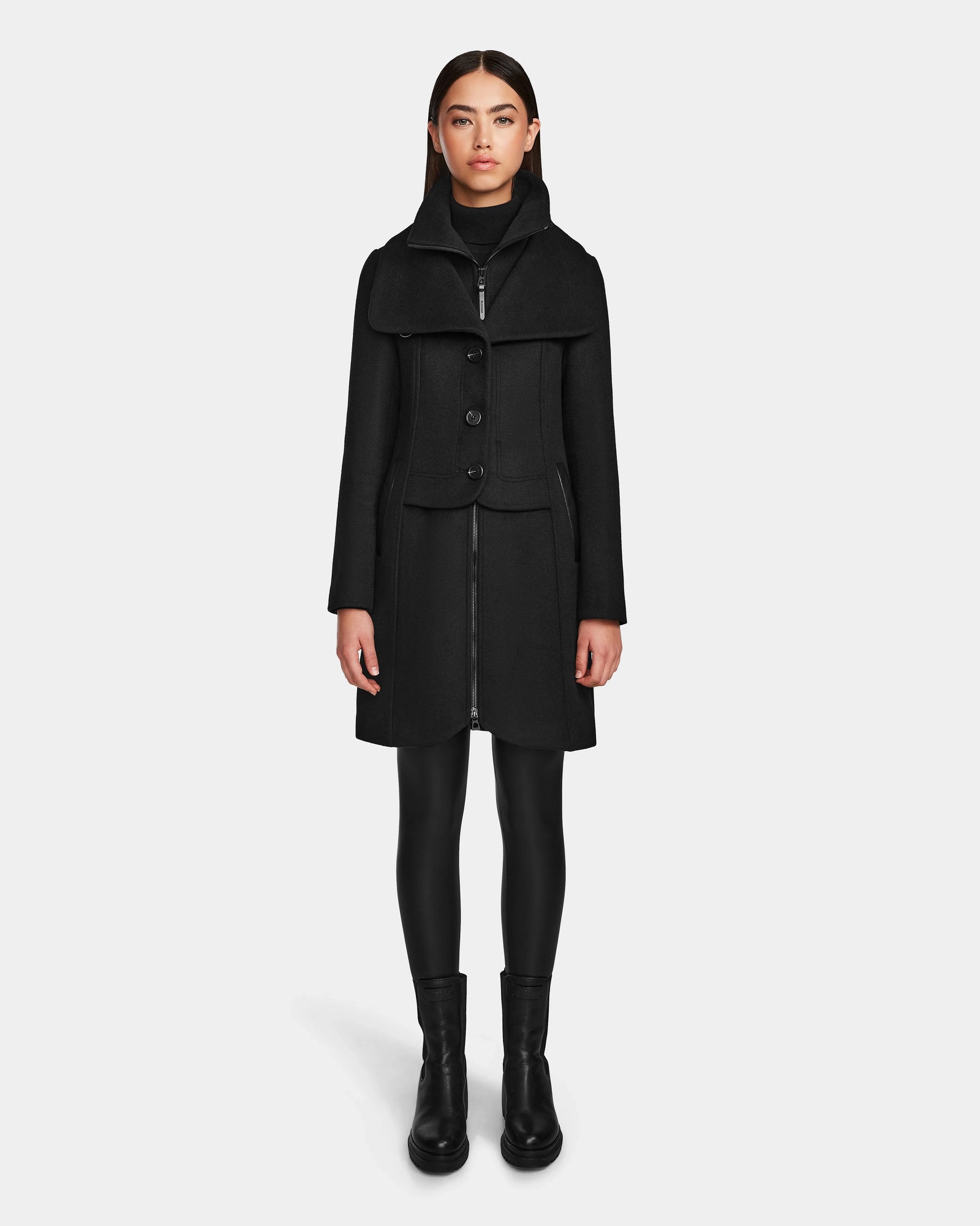 A woman faces forward wearing the Rudsak CAROLINE - L124543 Black knee-length premium wool blend coat, styled with a black turtleneck, leggings, and ankle boots against a plain white background.