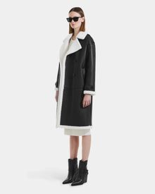 Wearing Rudsak’s DARCY - L125539 Black faux sherpa teddy coat, black sunglasses, a white dress, and black ankle boots, a woman stands against a plain white background.