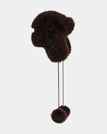 The DEMI - L425539 Espresso by Rudsak is a women's dark brown faux-fur aviator hat with ear flaps and two pom-poms on strings, shown against a plain light gray background.