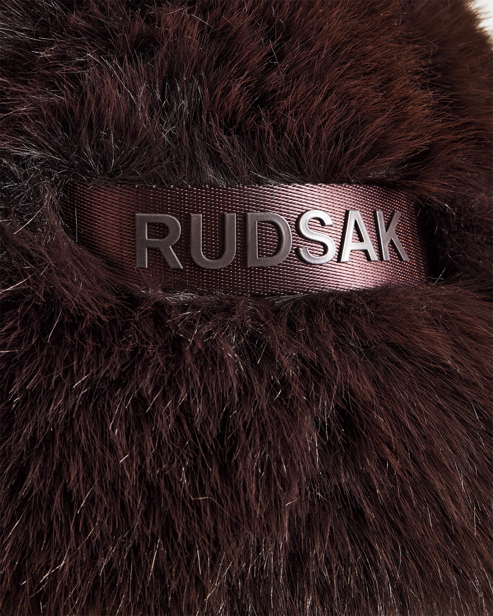Close-up of the Rudsak DEMI - L425539 Espresso women's faux-fur aviator hat in dark brown, featuring a black ribbon with metallic RUDSAK letters, highlighting the stylish winter accessory’s luxurious texture.
