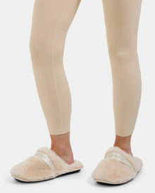 A person wearing beige leggings and Rudsak FLUFF - L223509 Cream faux-fur slippers with a white strap that reads RUDSAK, standing on a white background.
