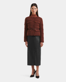 A woman faces forward in a Rudsak FRANCESCA - 8125021 Rust fitted brown quilted puffer jacket with buttons and pockets, a black midi skirt with a vegan leather belt, and black pointed heels against a plain white background.